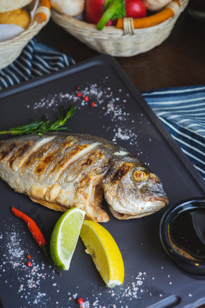 Grilled fish on a plate with a glass of wine and baked vegetables.の写真素材