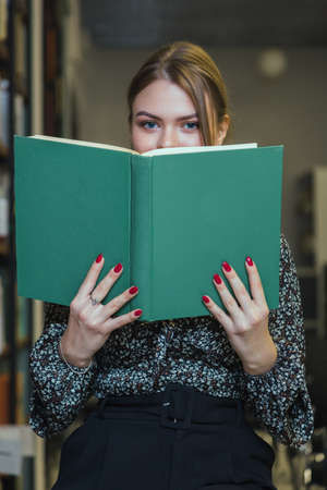 Girl is studying a book next to the rows of bookshelves.の写真素材