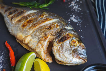 Grilled dorado fish on a plate with vegetables, lemon and a glass of white wine.の写真素材