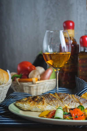 Grilled white fish on a dish on a table in a restaurant with a glass of white wine.の写真素材
