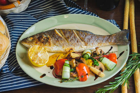 Grilled white fish on a dish on a table in a restaurant with a glass of white wine.の写真素材