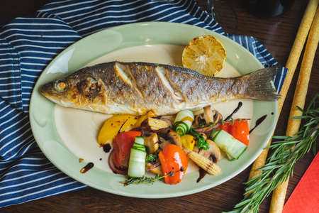 Grilled white fish on a dish on a table in a restaurant with a glass of white wine.の写真素材