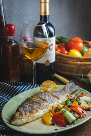 Grilled white fish on a dish on a table in a restaurant with a glass of white wine.の写真素材