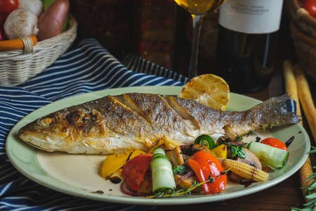 Grilled white fish on a dish on a table in a restaurant with a glass of white wine.の写真素材