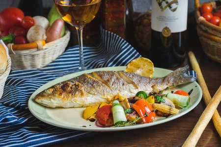 Grilled white fish on a dish on a table in a restaurant with a glass of white wine.の写真素材