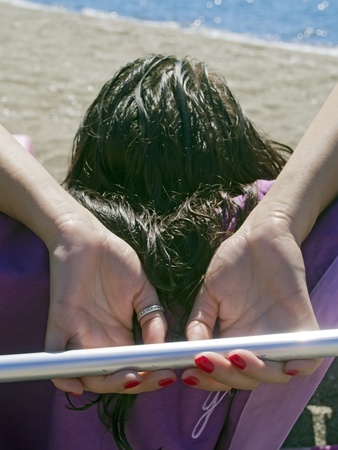 woman relaxes on a deck chair, on the beach, facing the seaの写真素材