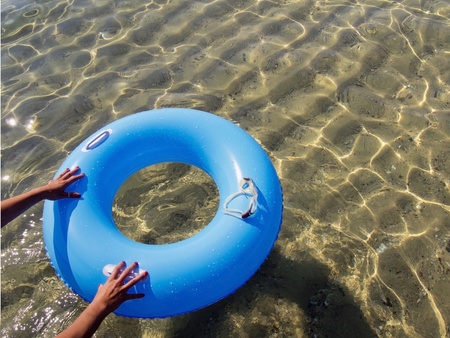 hands pushing a blue donut inflatable in the seaの写真素材