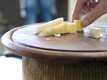 hand grasping cubes of cheese on a wooden cutting board ready for tastingの写真素材