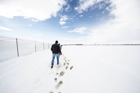 Bologna,Italy- people are trekking in a snowy countryside near a fenceの写真素材