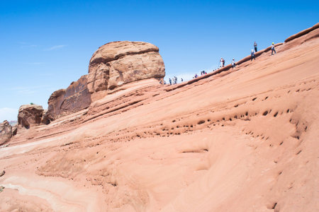 people walking inside the arches national park near the famous delicate arch during a sunny dayの写真素材