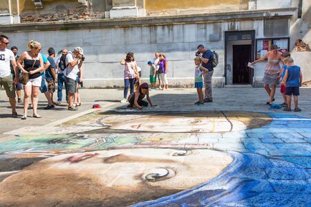 Venice,Italy-August 12,2014:Many people observe a young street artist drawing on the floor of a way the artistic figures during a sunny day in venice.のeditorial素材