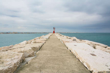 a red lighthouse  in front off the small port of Rimini during a cloudy day.