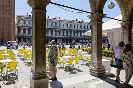 Venice,Italy -August 17,2014:people stroll in the famous saint Mark square in Venice near the bar with the yellow chairs during a sunny day.のeditorial素材