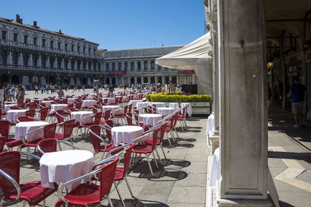 Venice,Italy -August 17,2014:people stroll in the famous saint Mark square in Venice near the bar with the red chairs during a sunny day.のeditorial素材
