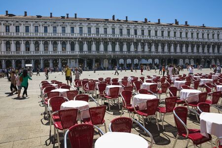 Venice,Italy -August 17,2014:people stroll in the famous saint Mark square in Venice near the bar with the red chairs during a sunny day.のeditorial素材