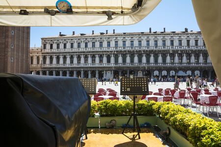 Venice,Italy -August 17,2014:people stroll in the famous saint Mark square in Venice near the bar with the red chairs during a sunny day.のeditorial素材