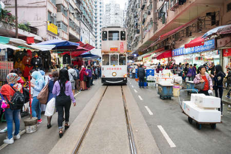 Hong Kong,March 24,2019:One of Hong Kong's many trams called Ding Ding runs through a crowded market during a cloudy day.のeditorial素材
