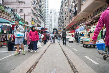 Hong Kong,March 24,2019:One of Hong Kong's many trams called Ding Ding runs through a crowded market during a cloudy day.のeditorial素材