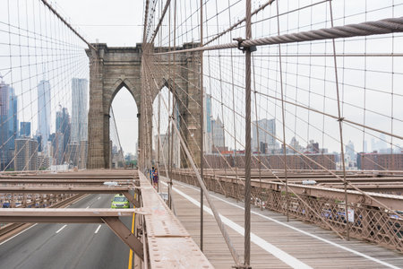 New York City, USA - August 6, 2019: People walk across the famous Brooklyn Bridge during a cloudy day.のeditorial素材