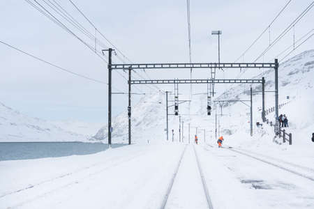 Hospice bernina, Switzerland-november 2, 2018: workers clean the tracks from snow in the train station of Hospice bernina along the way of the red train of the bernina during a cloudy day.のeditorial素材