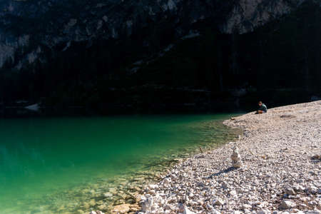 Braies, Italy-September 10, 2021: boy sitting on the shore of Lake Braies in the province of Bolzano admires the mountains that surround him during a sunny dayのeditorial素材