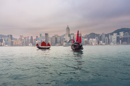 Hong Kong,March 25,2019:View of the Hong Kong skyscrapers and traditional boat from the Avenue of star on the Victoria Harbor during a cloudy dayのeditorial素材