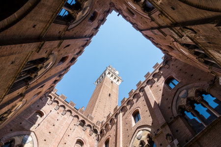 Siena,Italy-August 10, 2020:view of the Mangia tower in piazza del campo from the internal courtyard of the civic museum during a sunny dayのeditorial素材