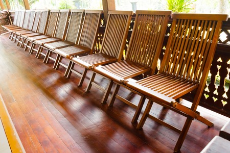 Empty wooden folding chairs are arranged sideways on the wooden floor. The chairs are brown colored.の写真素材