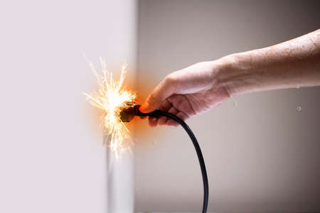 Wet hand connecting electrical plug cause electric shock, Idea for causes of home fire, Electric short circuit, Electrical hazard can ignite household items, Residential building electrical fires.の写真素材