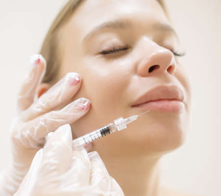 The beautician makes the patient augmentation of the lips with the help of injections of the hyaluronic acid fillerの写真素材