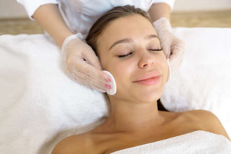 The beautician cleans the face from cosmetics to the patient before the procedureの写真素材