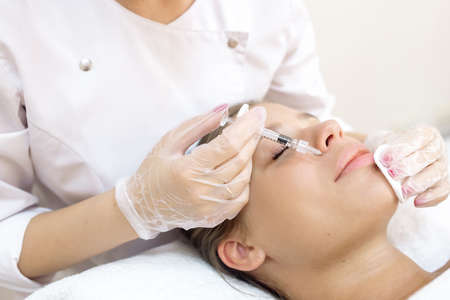 The beautician makes the patient augmentation of the lips with the help of injections of the hyaluronic acid fillerの写真素材