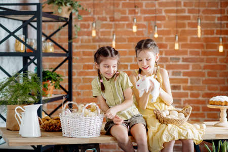Two little sisters at the Easter table are playing with chickens and ducklings and Easter bunnies....