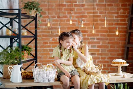 Two little sisters at the Easter table are playing with chickens and ducklings and Easter bunnies. Cute concept for easterの写真素材