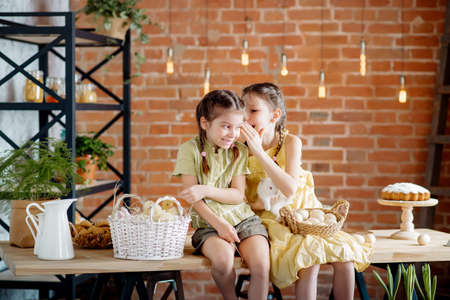 Two little sisters at the Easter table are playing with chickens and ducklings and Easter bunnies. Cute concept for easterの写真素材
