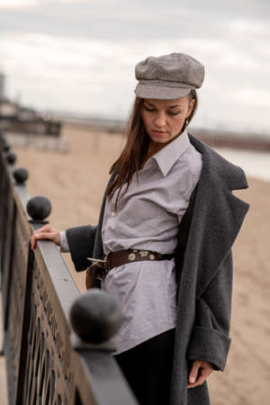 A beautiful young brunette woman walks on the beach in cool weather in a fashionable outfitの写真素材