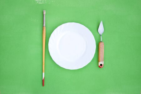 White plate with paintbrush and a palette knife on bright green backgroundの写真素材