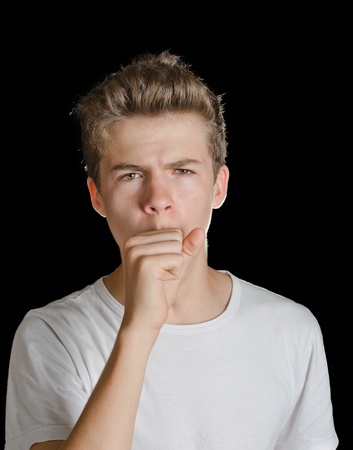 Cute teenager boy coughing with hand in front of his mouth, isolated on blackの写真素材
