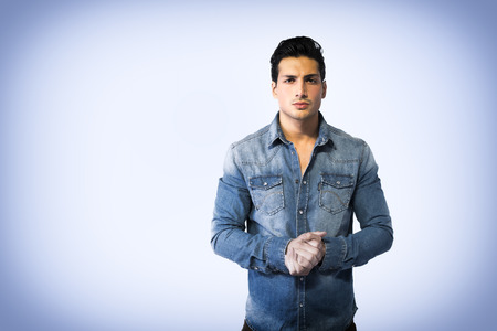 Young man wearing denim shirt, hands joined together, looking right at cameraの写真素材