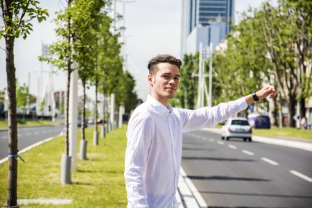 Young handsome man on side of a road, hailing and stopping a taxi cabの写真素材