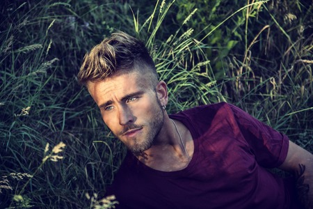 Good looking, blue eyed male model relaxing lying on the grass, looking to a side, photographed right from aboveの写真素材