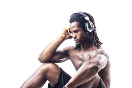 Handsome shirtless muscular black bodybuilder man listening to music with headphones in studio shot isolated on white backgroundの写真素材