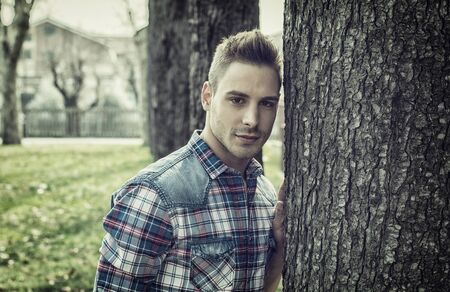 A young man outdoors against a tree, at sunset, with sun behind him, shot from belowの写真素材