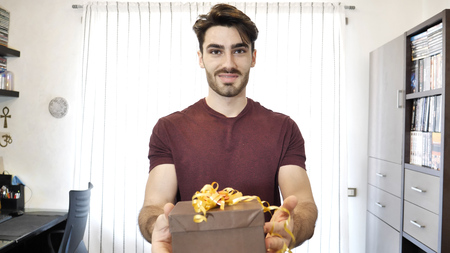 Smiling handsome surprised young man receiving or giving small gift.の写真素材