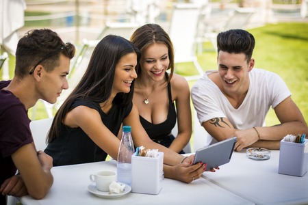 Young handsome stylish men and beautiful women sitting at table looking at tablet screen.