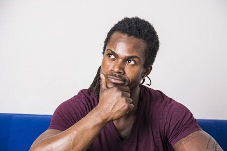 Handsome unsure, doubtful black man thinking, looking up with dubious expression on his faceの写真素材