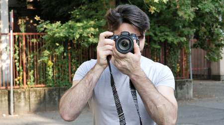 Handsome young male photographer taking photograph with professional photo camera hanging from his...