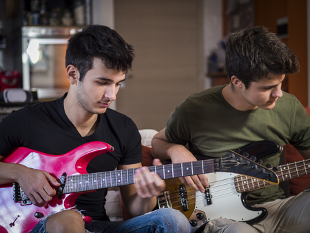 Two casual guys posing on sofa and playing electric guitars in band.の写真素材