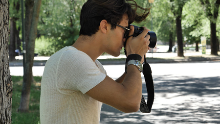 Handsome young male photographer taking photograph with professional photo camera hanging from his...