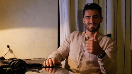 Excited or happy attractive young businessman sitting at desk with computer at home winking to the...